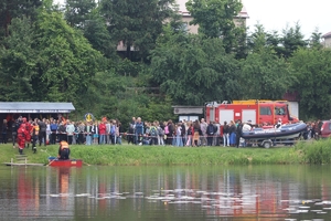 Na zdjęciu na pierwszym planie rozlewisko wodne w tle wóz strażacki i uczestnicy pokazu.