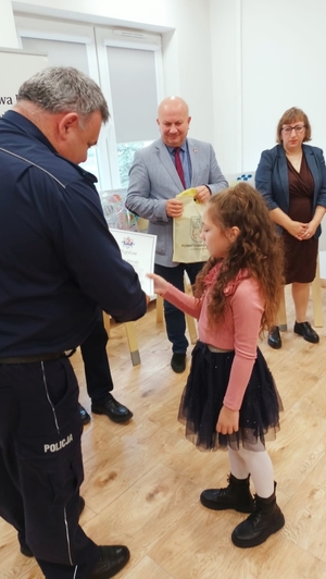 Na zdjęciu dziewczynka, laureatka konkursu otrzymuje dyplom i nagrodę od Komendanta Powiatowego policji w Lubaczowie oraz władz samorządowych.