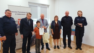 Na zdjęciu laureat konkursu z nagrodą w postaci plecaka oraz dyplomem obok niego Komendant powiatowy policji w Lubaczowie oraz władze samorządowe.