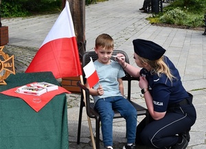 Na zdjęciu policjantka w umundurowaniu służbowym malująca dziecku flagę.