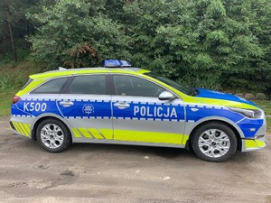 Na zdjęciu znajduje się radiowóz z napisem Policja. W tle drzewa koloru zielonego. Pojazd jest zaparkowany w miejscu wyznaczonym do parkowania.