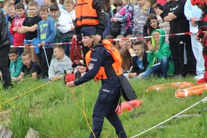 Na zdjęciu policjantka w mundurze służbowym rzuca do wody line ratunkową.