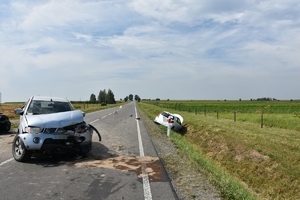 Na zdjęciu zdarzenie drogowe, pojazd koloru srebrnego stojący na drodze z widocznymi uszkodzeniami części czołowej pojazdu, w tle pojazd koloru białego.