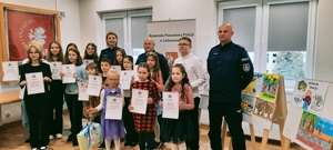Policjanci w umundurowaniu oraz laureaci konkursu w nagrodami i dyplomami.