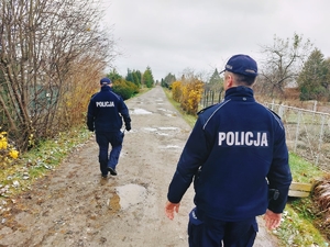 Na zdjęciu policjanci w umundurowaniu służbowym patrolują teren ogródków działkowych.