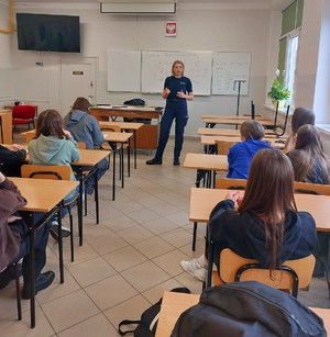 Zdjęcie przedstawia policjantkę w umundurowaniu służbowym oraz uczestników spotkania.