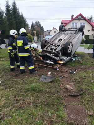 Zdjęcie przedstawia dwóch strażaków oraz samochód znajdujący się na dachu.