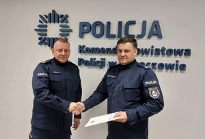 Na zdjęciu dwóch policjantów w umundurowaniu służbowym. W tle logo Komendy Powiatowej Policji w Lubaczowie.