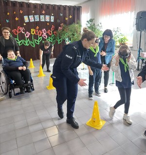 Na zdjęciu policjantka w umundurowaniu służbowym oraz dzieci przechodzące po torze przeszkód w magicznych okularach.