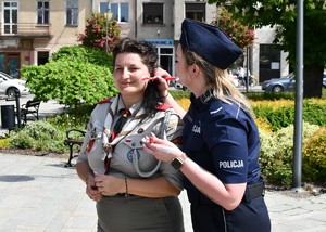 Na zdjęciu umundurowana policjantka malująca harcerce na twarzy biało-czerwoną flagę.