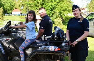 Na zdjęciu policjant i policjantka w umundurowaniu służbowym i dzieci siedzące na quadzie.