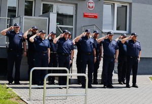 Na zdjęciu policjanci w umundurowaniu służbowym oddający hołd zmarłemu  żołnierzowi w tle budynek komendy.