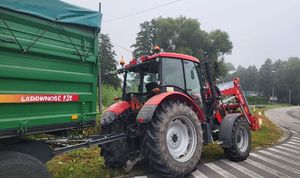 Na zdjęciu ciągnik rolniczy z naczepą stojący na jezdni.