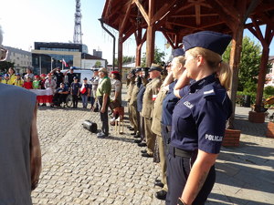 Na zdjęciu stojące policjantki w umundurowaniu służbowym harcerze i zuchu stoją na płycie rynku.