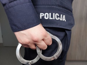 Na zdjęciu ręka trzymająca kajdanki na tle napisu policja.