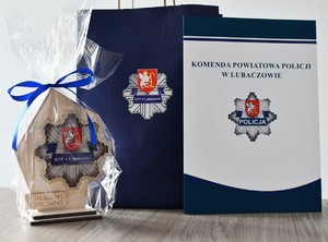 Statuetka z logo KPP Lubaczów i napisem pomagamy i chronimy, torba prezentowa z logo KPP Lubaczów oraz teczka z napisem Komenda Powiatowa Policji w Lubaczowie.