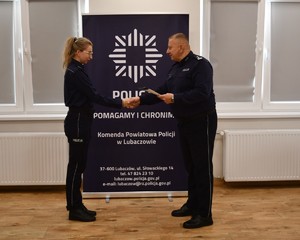 Na zdjęciu policjantka otrzymujący świadectwo oraz Komendant, w tle napis Komenda Powiatowa Policji w Lubaczowie.