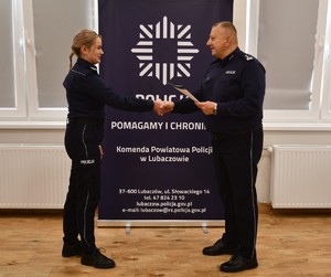 Na zdjęciu policjantka otrzymujący świadectwo oraz Komendant, w tle napis Komenda Powiatowa Policji w Lubaczowie.