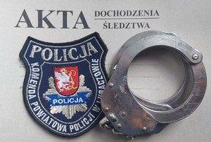 Na zdjęciu akta sprawy, kajdanki i emblemat z logiem i napisem Komenda Powiatowa Policji w Lubaczowie.