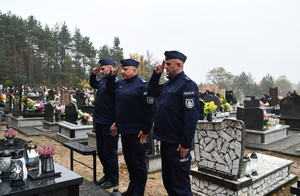 Na cmentarzu Komendant Powiatowy Policji w Lubaczowie oraz przedstawiciele kadry kierowniczej oddają hołd. W tle groby. Policjanci występują w umundurowaniu służbowym.