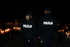 Policjanci w umundurowaniu służbowym, noc, w tle palące się znicze.