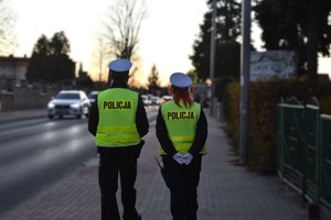 Policjanci w umundurowaniu służbowym, idą chodnikiem przy ruchliwej ulicy.