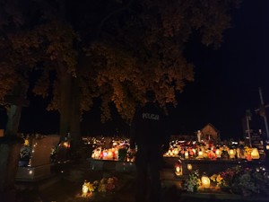 Na zdjęciu cmentarz nocą, w centralnej części stoi policjant w umundurowaniu służbowym.