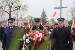 Delegacja służb mundurowych w umundurowaniu służbowym trzy osoby niesie wiązankę kwiatów.