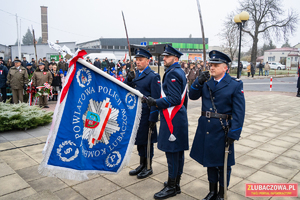 Poczet sztandarowy policji w umundurowaniu służbowym wraz z sztandarem w postawie na baczność.