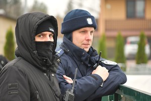 Umundurowany funkcjonariusz policji obok niego w kominiarce funkcjonariusz pionu kryminalnego.