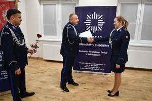 Komendant i Zastępca w umundurowaniu galowym stoją na auli. Komendant wręcza akt mianowania policjantce.