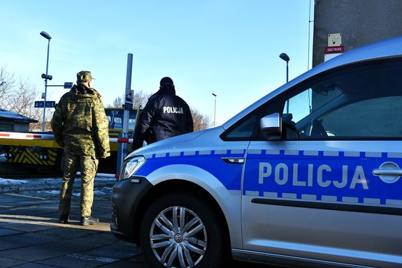 Policjant i strażnik graniczny oraz radiowóz policyjne przy torach.