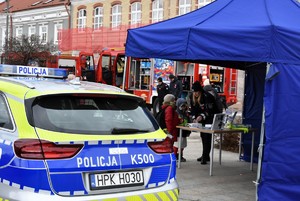 W namiocie stoi policjantka i dzieci. Obok radiowóz.