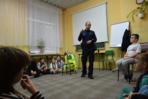 Dzieci uczestniczące w spotkaniu i policjant w umundurowaniu służbowym.