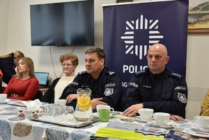 Dwóch policjantów w umundurowaniu służbowym i dwie kobiety siedzą przy stole.