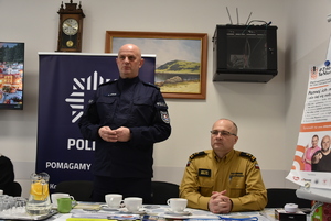 Policjant stojący i siedzący strażak w umundurowaniu służbowym.