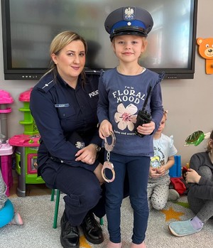 Policjantka i dziewczynka w czapce policyjnej trzymająca kajdanki.