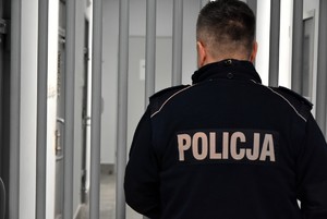 Policjant stojący przed okratowanym wejściem do cel.