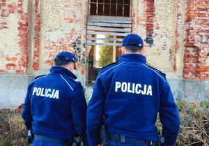 Na tle budynku dwóch policjantów w umundurowaniu służbowym.