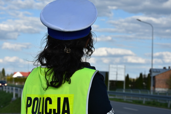 Policjantka w umundurowaniu służbowym w białej czapce i kamizelce odblaskowej.