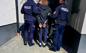 mężczyzna w kajdankach i umundurowani policjanci.