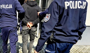 mężczyzna w kajdankach i umundurowani policjanci.