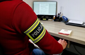 Postać z emblematem 'POLICJA' przy komputerze.